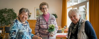 Drei Seniorinnen lächeln in die Kamera.