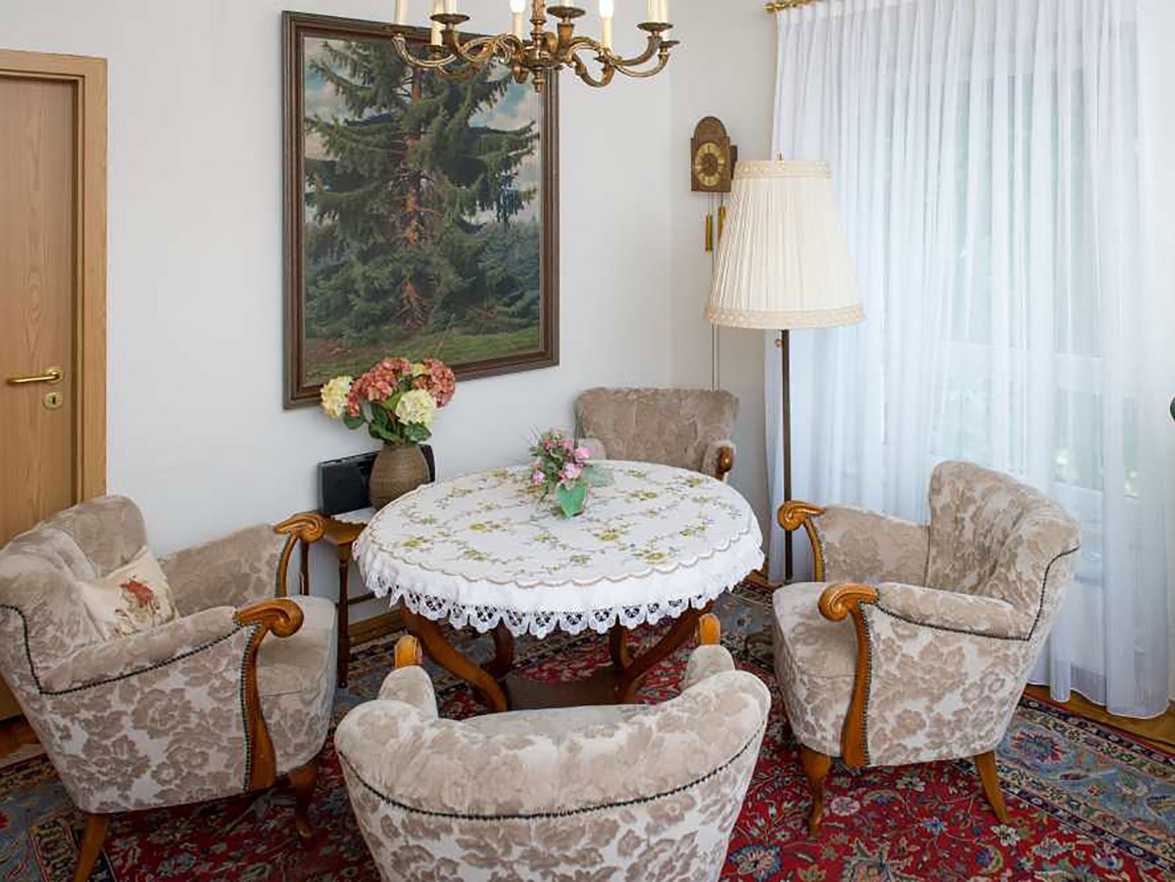 Aufenthaltsraum mit Sesseln, rundem Tisch, Kronleuchter und Gemälde an der Wand