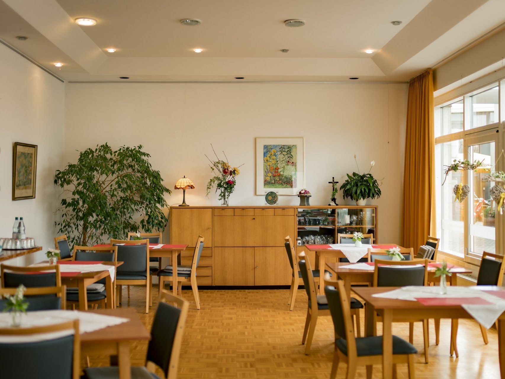 Das Foto zeigt ein helles, freundliches Esszimmer mit vielen Pflanzen und schönen Holzmöbeln.