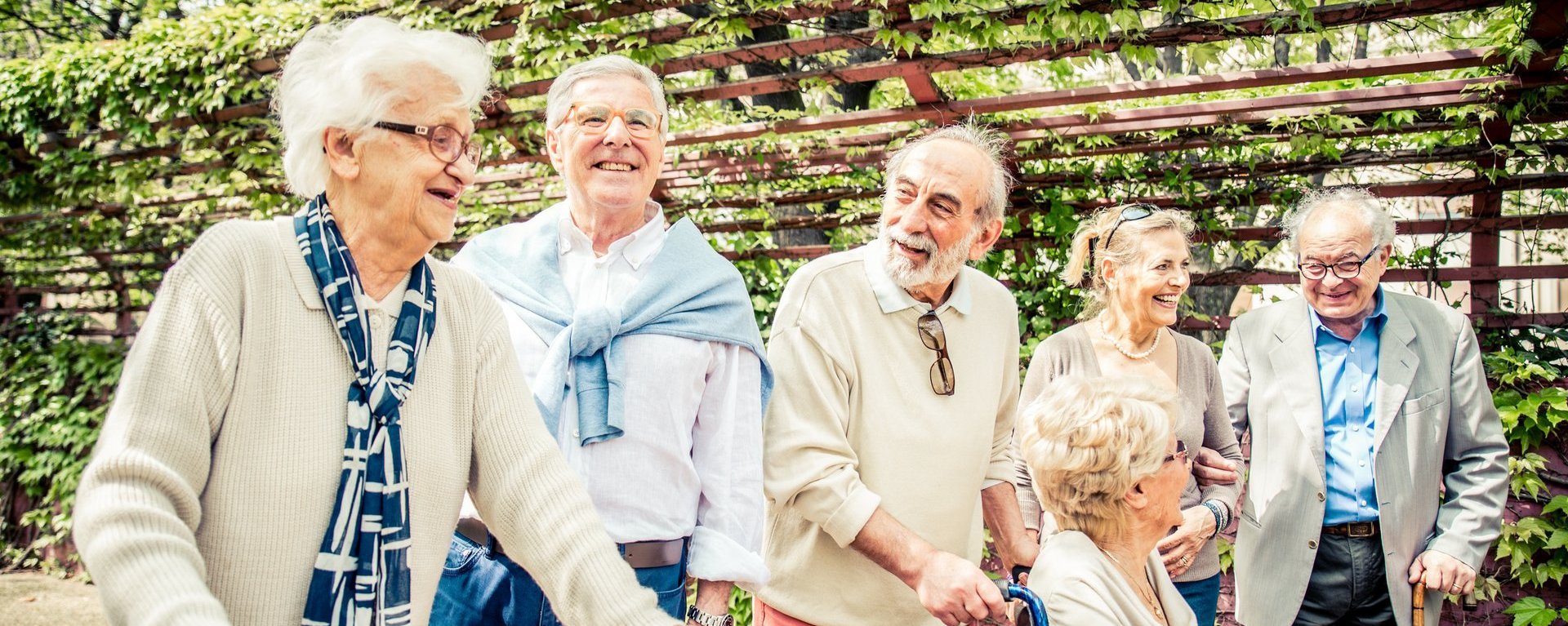 Eine Gruppe Bewohner teilw. im Rollstuhl und mit Gehhilfe im Garten - alle sind fröhlich