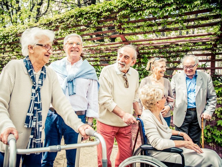 Eine Gruppe Bewohner teilw. im Rollstuhl und mit Gehhilfe im Garten - alle sind fröhlich