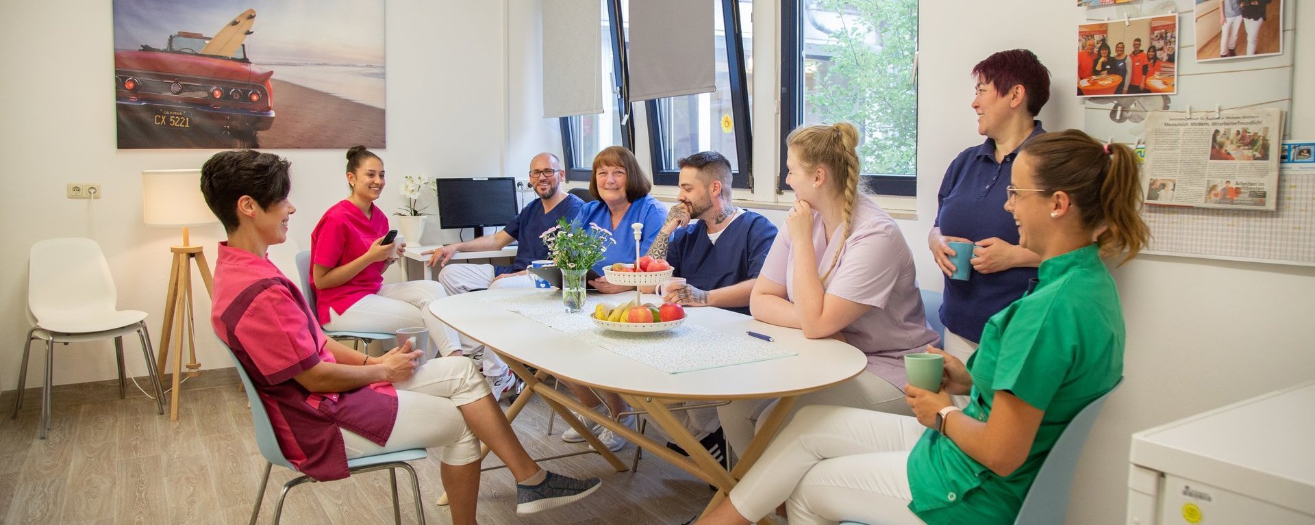 Eine Gruppe Pflegekräfte sitzen um einen Tisch im Aufenthaltsraum, sprechen und lachen