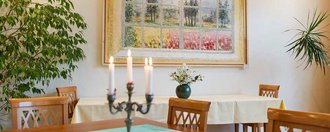Kerzen im Vordergrund auf einem Tisch mit Holzstühlen - Gemälde mit Naturbild im Hintergrund